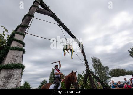Klockenhagen, Germania. 27 luglio 2024. Un cavaliere batte una boa di aringhe con un club. Gareggia con altri quindici cavalieri per diversi titoli reali alla tradizionale battuta a botte a Klockenhagen. Nel 2017, la pratica diffusa di battere il barile sul Mar Baltico è stata aggiunta all'elenco del patrimonio culturale immateriale dell'UNESCO. Crediti: Stephan Schulz/dpa/Alamy Live News Foto Stock