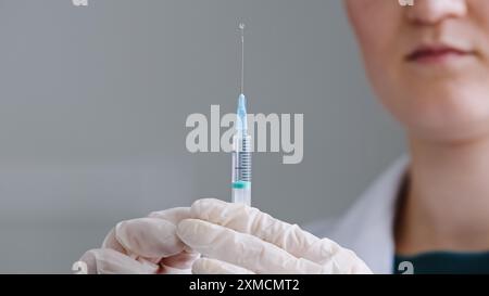 Donna irriconoscibile medico infermiere operatore medico scienziato indossa guanti in lattice tiene siringa con ago in mani schizzi di antibiotico liquido Foto Stock