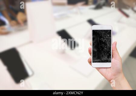 tenere a mano il telefono cellulare con schermo in vetro rotto e negozio elettronico di sfocatura astratta per la riparazione dello smartphone Foto Stock