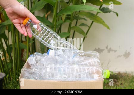 Tenere le mani e inserire i flaconi di plastica nella scatola marrone per rifiuti Foto Stock