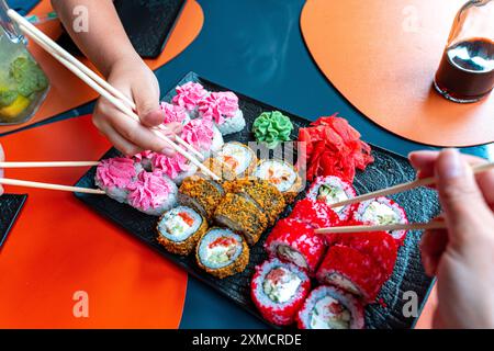 Panini di sushi e persone con bacchette cinesi in mano prendono sushi. Ristorante Giapponese, piatto nero con panini assortiti al forno e Philadelphia Foto Stock
