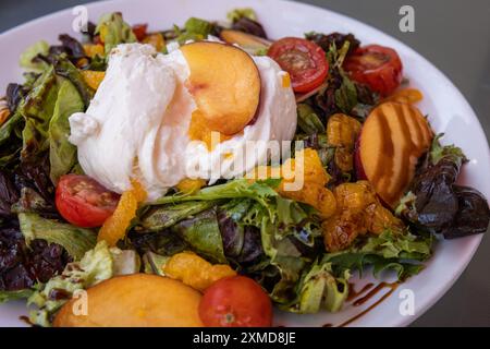 Insalata estiva con burrata fresca e pesche di stagione. L'insalata ha molti ingredienti diversi, tra cui pomodori, arance e lattuga Foto Stock