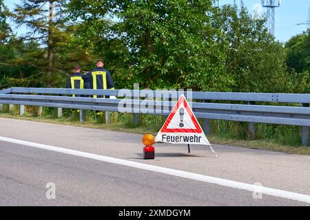 Autobahn A96, Baviera, Germania - 26 luglio 2024: un cartello segnaletico dei vigili del fuoco assicura un incidente sull'autostrada A96 tra Erkheim e Mindelheim mentre i vigili del fuoco lavorano sullo sfondo *** Ein Warnschild der Feuerwehr sichert eine Unfallstelle auf der Autobahn A96 zwischen Erkheim und Mindelheim ab, während Feuerwehrleute im Hintergrund tätig peccd Foto Stock