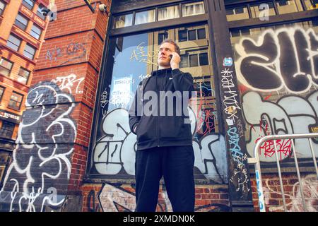 Manhattan, New York, USA, 18 aprile 2022. Un uomo in nero parla al telefono di fronte ad un edificio in mattoni con grafite sullo sfondo Foto Stock