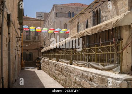 Uno stretto vicolo nella parte vecchia di Gerusalemme, Israele, con tipiche case in pietra e marciapiedi, e con colorati ombrelli decorativi. Foto Stock