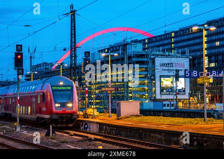 L'arco illuminato della Lanxess Arena di Deutz, treno sulla piattaforma della stazione ferroviaria Koelnmesse/Deutz, Renania settentrionale-Vestfalia, Germania Foto Stock