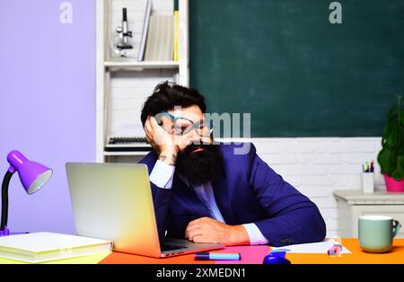 Stanco insegnante di scuola maschile che dorme sulla scrivania. Pausa scolastica. Studente universitario sovraccarico di lavoro in preparazione per la sessione d'esame. Sonnolenza e stanchezza. TIR Foto Stock