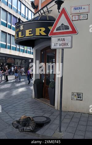 La scultura Cumil, il lavoratore delle fogne, sbircia fuori da un tombino in una strada pedonale nella storica città vecchia di Bratislava. Foto Stock