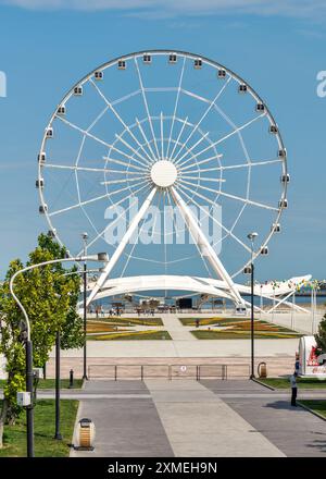 Baku, Azerbaigian - 4 maggio 2024: Una vista della ruota panoramica Baku Eye, situata accanto al centro commerciale Deniz. La ruota è sullo sfondo con poche persone che camminano in primo piano. Foto Stock