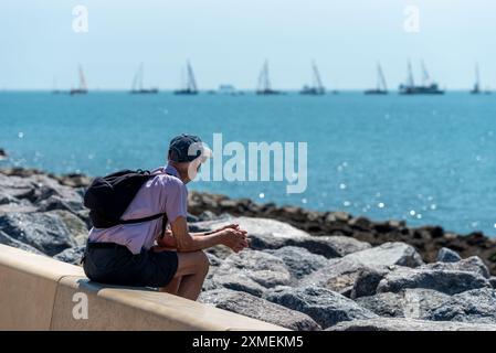 Un uomo anziano siede da solo sulle difese marine a Portsmouth, osservando navi e barche nel Solent in una calda giornata estiva. Luglio 2024. Foto Stock