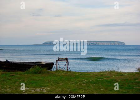 Paesaggio costiero sull'isola svedese di Gotland con una barca da pesca in legno sulla riva del Mar Baltico e con l'isola di Karlsö sullo sfondo. Foto Stock