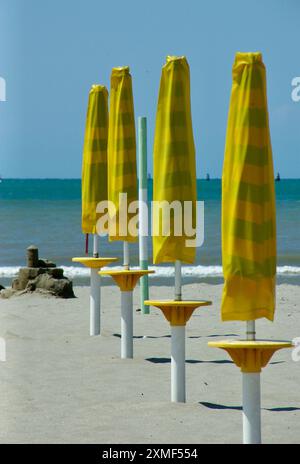 Spiaggia vuota con sabbia fine e ombrelloni gialli ripiegati sul mare Adriatico in Italia in estate. Foto Stock