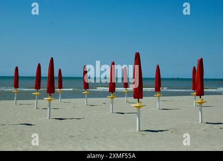 Spiaggia vuota con sabbia fine e ombrelloni rossi ripiegati sul mare Adriatico in Italia in estate. Foto Stock