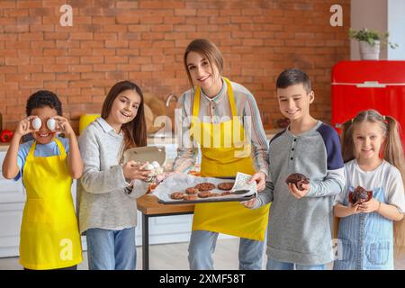 Chef donna con gruppo di bambini piccoli e pasticceria preparata dopo la lezione di cucina in cucina Foto Stock