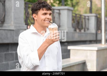 Bel giovane che beve delizioso latte ghiacciato all'aperto Foto Stock