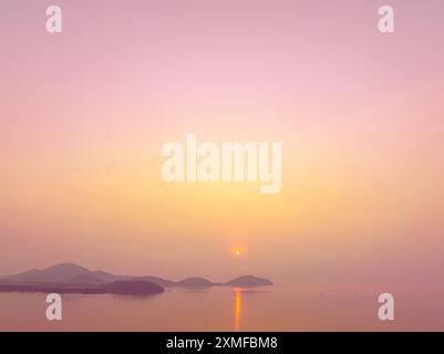 Vista aerea mozzafiato sul sole dorato che splende sopra l'isola. Scena di riflessioni colorate sul mare. il cielo dolce copre l'oceano. Col. Gradiente Foto Stock