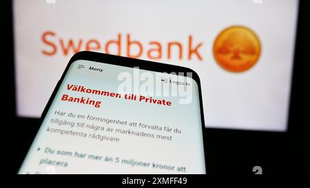 Smartphone con sito web della società svedese di servizi finanziari Swedbank AB davanti al logo aziendale. Mettere a fuoco in alto a sinistra sul display del telefono. Foto Stock