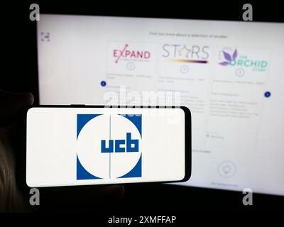 Persona che detiene un telefono cellulare con il logo della società biofarmaceutica belga UCB SA davanti alla pagina Web aziendale. Mettere a fuoco il display del telefono. Foto Stock