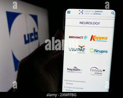 Persona che detiene lo smartphone con la pagina web della società biofarmaceutica belga UCB S.A. davanti al logo. Messa a fuoco al centro del display del telefono. Foto Stock