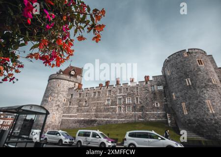 Windor Castle, Regno Unito - 16 ottobre 2023: Un muro del castello e torri con fiori rosa e arancio in primo piano. Foto Stock