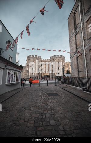 Windor Castle, Regno Unito - 16 ottobre 2023: Una strada acciottolata conduce ad un cancello del castello con gente che cammina verso di esso. Le bandiere britanniche sono appese in alto. Foto Stock