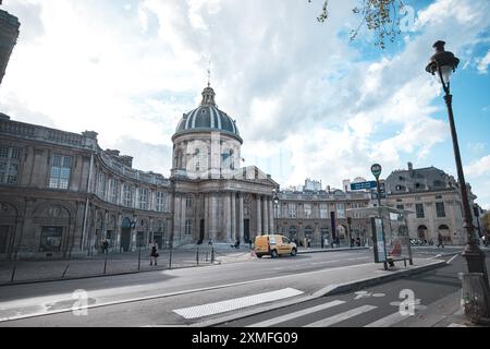Parigi, Francia - 19 ottobre 2023: Un grande edificio in pietra con tetto a cupola si erge accanto a una strada. Ci sono auto e persone in strada, e un bu Foto Stock