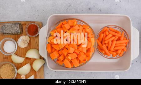 Ricetta per zuppa di zucca arrostita. Cubetti di zucca sbucciati e senza semi, carota, cipolla, aglio e spezie da vicino in una teglia da forno in ceramica inclusa nel kit Foto Stock