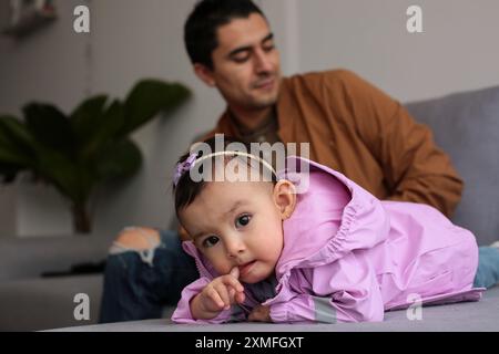 Il bambino carino gioca sul divano del soggiorno, sotto la supervisione di suo padre Foto Stock