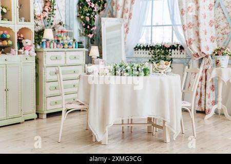 Accogliente sala da pranzo vintage, design floreale, mobili verdi e bianchi pastello, composizioni floreali sul tavolo, grande finestra, elementi decorativi, invitante Foto Stock
