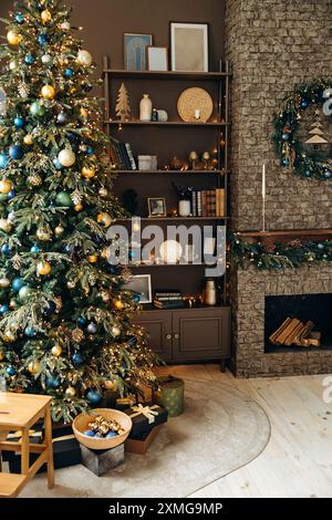 Grande albero di Natale decorato con molte palle di Natale e luci della ghirlanda in una sala accogliente con caminetto in mattoni e un'unità scaffale con libri e. Foto Stock