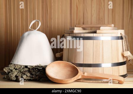 Frusta per sauna in quercia, cappello in lana di feltro, secchio e mestolo su una superficie in legno Foto Stock