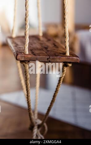Rustico altalena in legno in un'accogliente camera da letto in stile bohémien con luce soffusa da sera. Foto verticale. Foto Stock