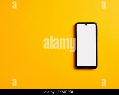 Modello smartphone con schermata bianca vuota su sfondo giallo. Vista superiore con spazio di copia. Foto Stock