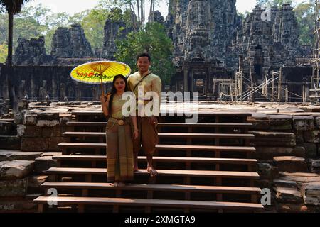 Coppia cambogiana sorridente in abiti tradizionali da matrimonio che posa sui gradini di legno del Tempio di Bayon ad Angkor, in Cambogia. Foto Stock