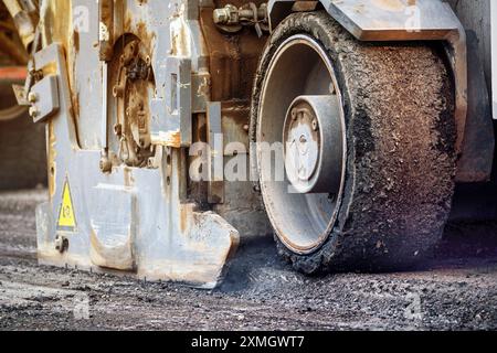 Primo piano di una pavimentazione asfaltata che posa un nuovo fondo stradale, mostrando i macchinari edili in azione. Foto Stock