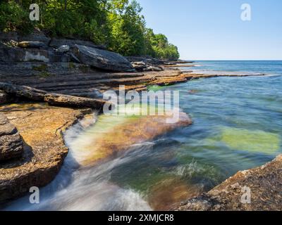 Scintillanti cascate d'acqua lisce sopra scogliere illuminate dal sole drappeggiate nel muschio del lago Ontario al Robert G. Wehle State Park, a nord dello stato di New York, incorniciate da un tranq Foto Stock