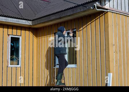 Lavori all'aperto sulle aperture delle finestre, il conciatetto installa le pendenze delle finestre metalliche sulla facciata della casa di campagna con pannelli di intelaiatura. Foto Stock