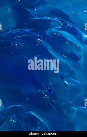 Primo piano della consistenza del gel dei prodotti cosmetici. crema trasparente su sfondo blu scuro con bolle. Foto Stock