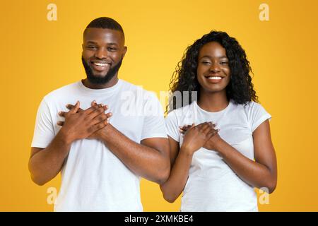 Sorridente afro l uomo e la donna mettendo le mani sui loro cuori Foto Stock