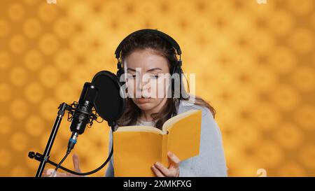 La donna fa la voce fuori campo leggendo libri per produrre audiolibri usando la recitazione drammatica. Il narratore utilizza abilità narrative e suoni espressivi mentre produce registrazioni di romanzi, background in studio, camera A. Foto Stock