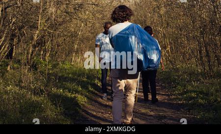 Persone soddisfatte che lasciano il bosco dopo una sessione produttiva di pulizia dei rifiuti, riuscendo a pulire l'ambiente forestale da rifiuti spazzatura e plastica. Attivisti felici e orgogliosi. Telecamera B.. Foto Stock