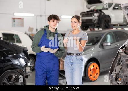 Giovane meccanico di auto che parla con una donna proprietaria di auto in officina Foto Stock