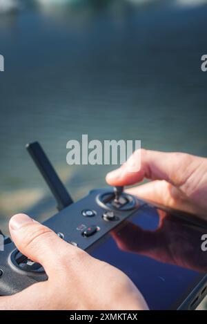 Primo piano delle mani che azionano il controller dei droni con acqua in background Foto Stock