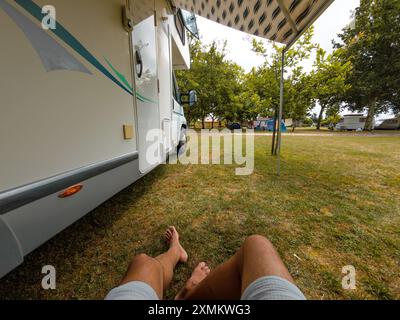 Rilassatevi seduti sotto la tenda sull'erba fuori dal camper nella ripresa verticale del campeggio Foto Stock