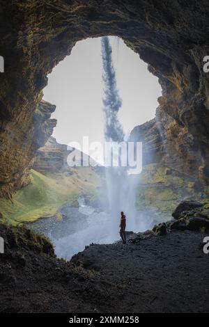 Figura sagomata dietro la cascata Seljalandsfoss con le lussureggianti Green Hills Foto Stock