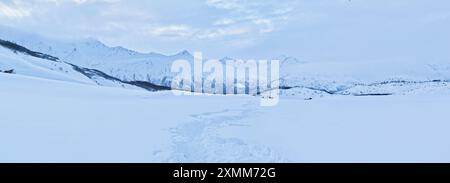 Cammina attraverso la neve profonda con montagne sullo sfondo in una giornata invernale vicino a Castner Cave in Alaska. Foto Stock