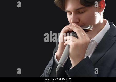 Artista maschile che suona armonica su sfondo scuro, primo piano Foto Stock