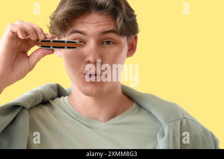 Giovane felice con armonica su sfondo giallo, primo piano Foto Stock