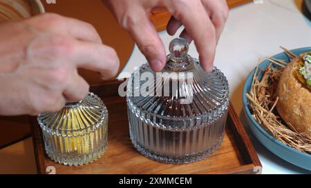 Mani eleganti che posizionano il vaso decorativo in vetro con coperchio accanto a quello più piccolo Foto Stock