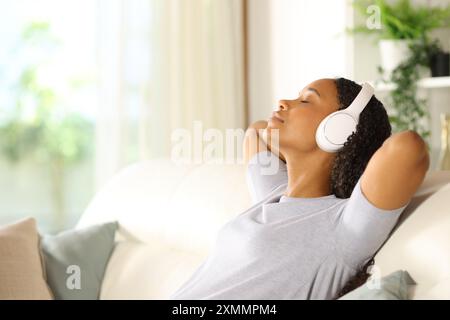 Visualizzazione laterale del ritratto di una donna nera che indossa le cuffie per ascoltare musica e rilassarsi a casa Foto Stock